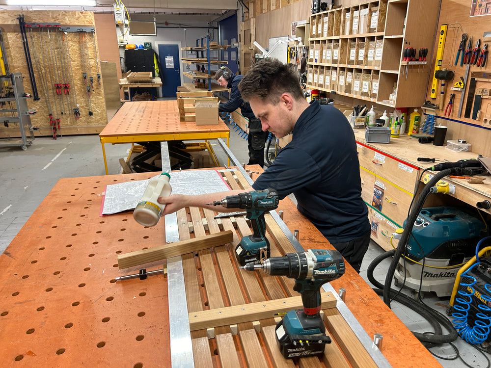 Person using a drill on wooden planks in a workshop setting
