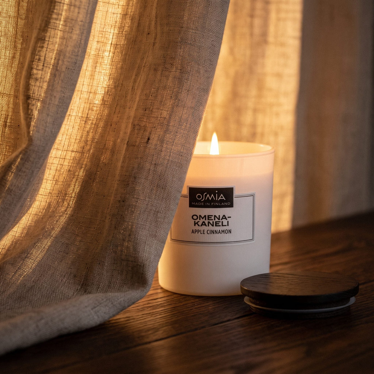 Apple-Cinnamon Scented Candle by Osmia - lit behind linen curtain