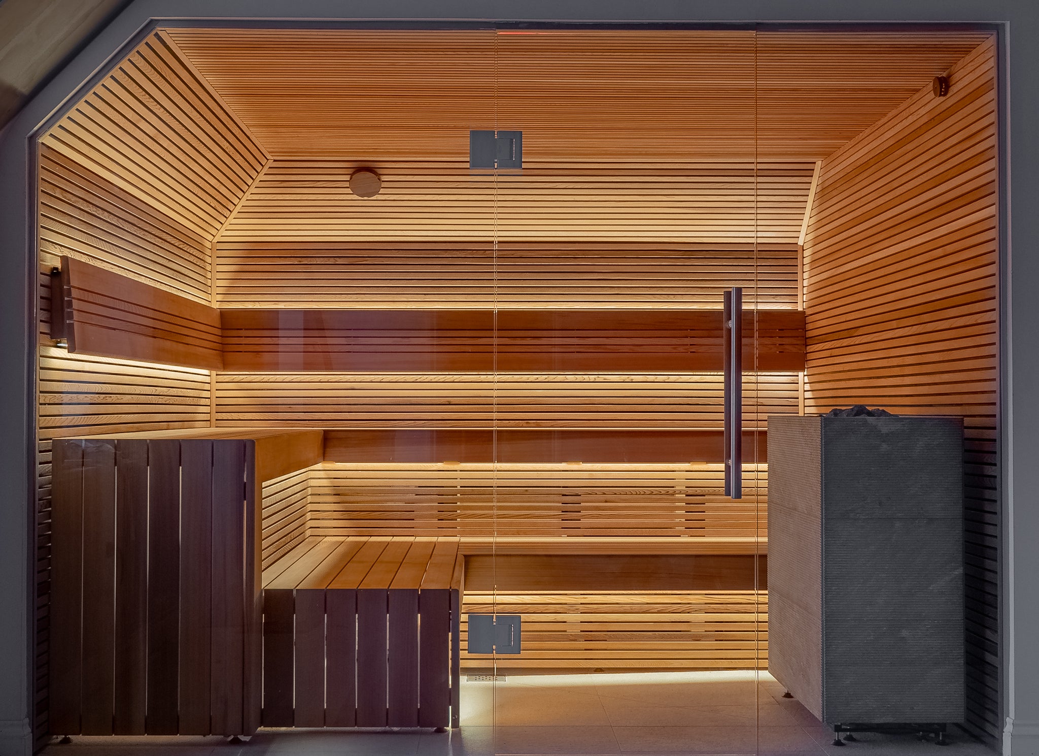 Bespoke Sauna Installation by Finnmark Sauna in Western Red Cedar with Tulikivi Tuisku XL sauna heater. The cladding is slatted red cedar boards mounted with a shadow gap and the sauna bench system has a waterfall edge mitre.