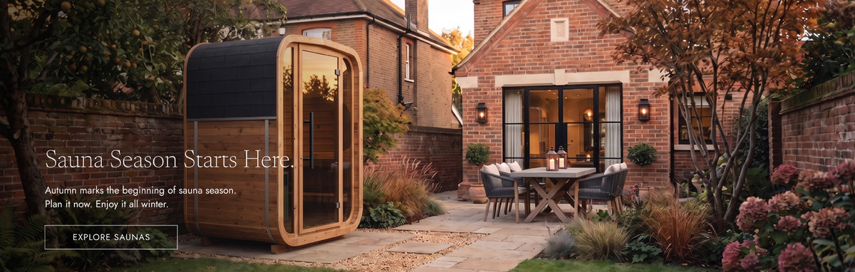 A modern outdoor sauna cabin with large glass windows and a dark curved roof stands beside a brick patio and dining set in a residential backyard. Text on the left reads 'Sauna Season Starts Here.