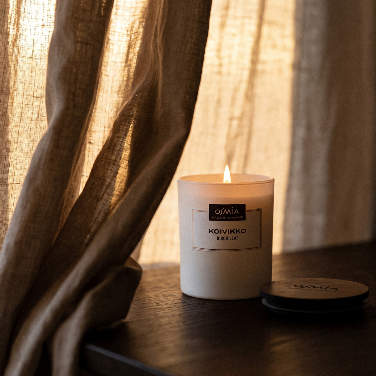 Birch Leaf Scented Candle (Koivikko) by Osmia - lit behind linen curtain