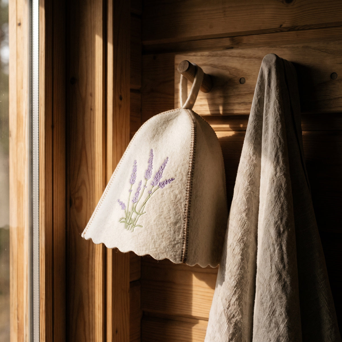 White Felt Sauna Hat with Lavender Embroidery - hanging on a sauna peg